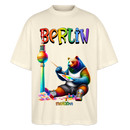 Illustration eines bunten Bären in Regenbogenfarben, der mit Pinsel und Farbpalette kreativ ist, vor dem Berliner Fernsehturm in Regenbogenoptik. Darüber der Schriftzug "Berlin" in Regenbogenfarben und darunter ganz klein "Findickjut". Perfekt zur Feier des CSD Berlin 2025. Oversized Unisex Bio T-Shirt -Naturweiß