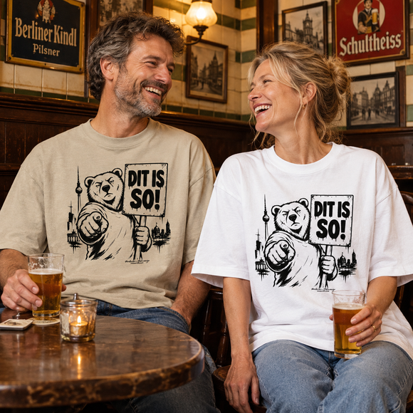 Zwei lachende Erwachsene in einer gemütlichen Berliner Altstadt-Kneipe tragen oversized T-Shirts mit dem Berliner Bärenmotiv „Dit is so!“. Ein Shirt ist beige, das andere weiß bedruckt.