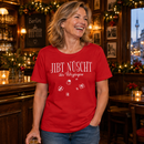 Lachende Frau zwischen 45 und 60 Jahren in einer weihnachtlich geschmückten Berliner Kneipe mit rotem Bio-Damen-T-Shirt und weißem „JIBT NÜSCHT, ihr Flitzpiepen“-Weihnachtsmotiv samt Geschenk-Illustrationen.