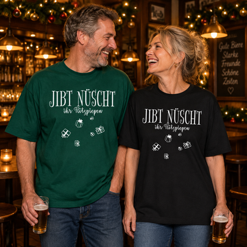 Lachendes Paar in einer weihnachtlich geschmückten Berliner Kneipe: Mann im grünen und Frau im schwarzen relaxed fit Bio-T-Shirt mit weißem „JIBT NÜSCHT, ihr Flitzpiepen“-Weihnachtsmotiv und Geschenk-Illustrationen.