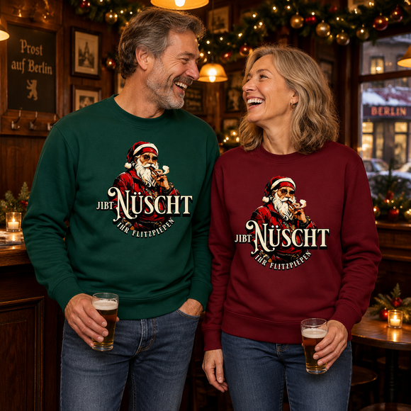 Lachendes Paar in einer weihnachtlich geschmückten Berliner Kneipe: Mann im grünen und Frau im burgunderroten Bio-Sweater mit Berliner Gangster-Weihnachtsmotiv, rauchendem Weihnachtsmann und dem Schriftzug „JIBT NÜSCHT, ihr Flitzpiepen“.